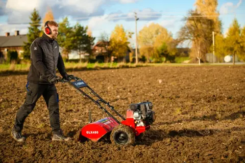 Mężczyzna w słuchawkach pracuje czerwoną glebogryzarką na polu.