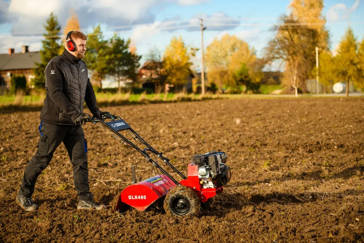 Mężczyzna w słuchawkach pracuje czerwoną glebogryzarką na polu.