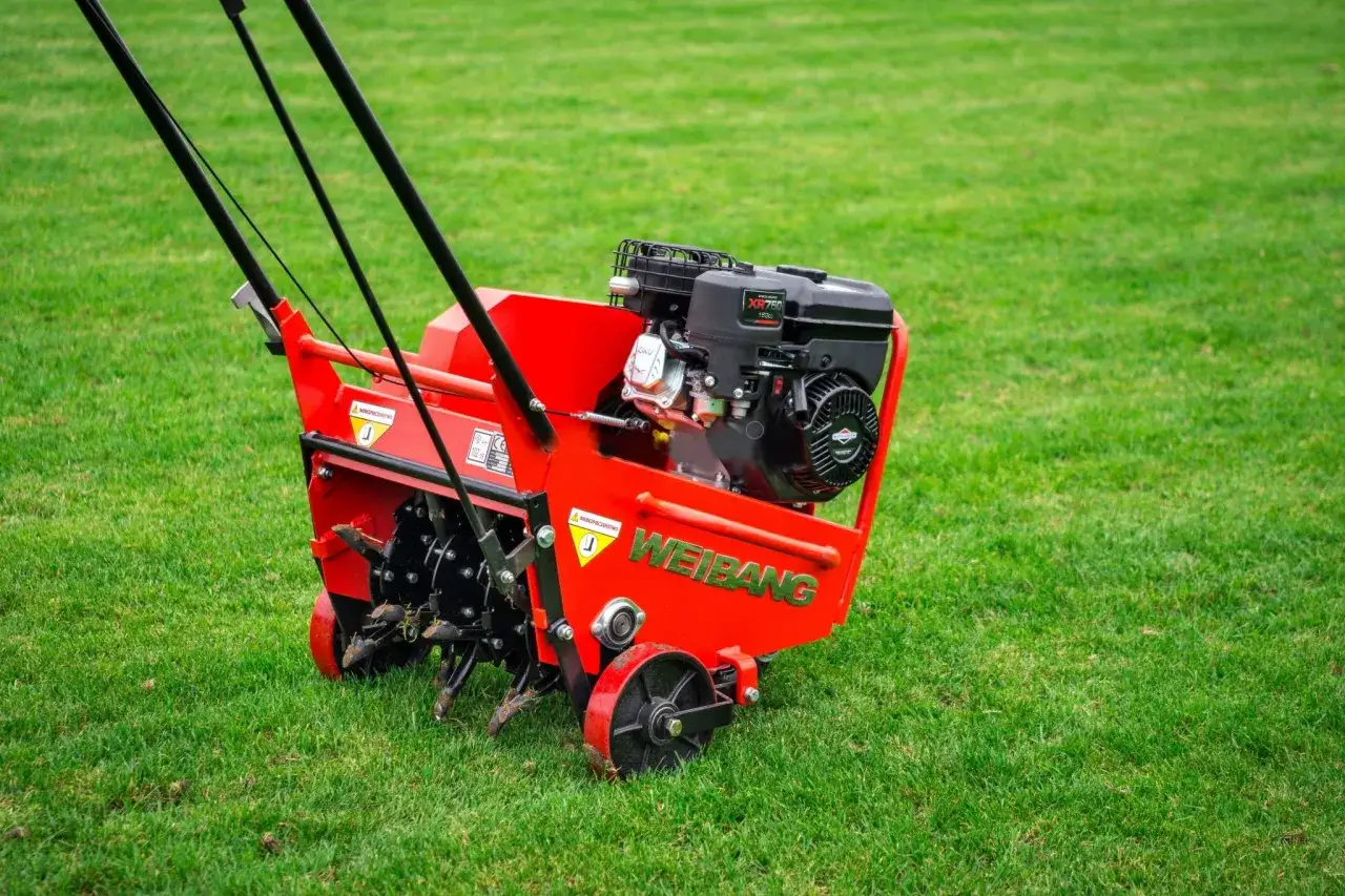 Czerwony aerator Weidemann na zielonej trawie. Idealny sprzęt, gdy robic aerację trawnika, by zapewnić mu zdrowszy wygląd.