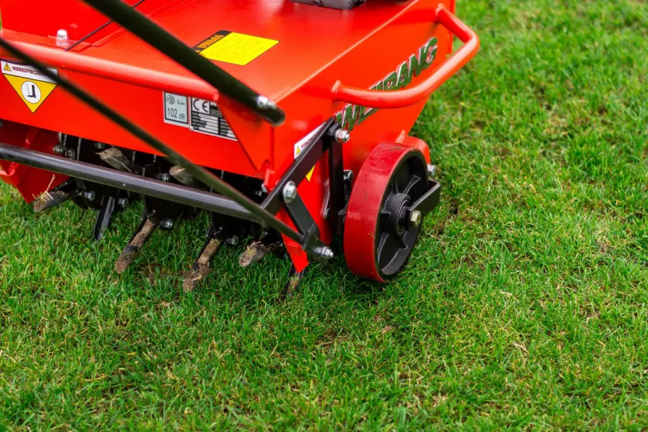 Czerwony aerator z kolcami wbijającymi się w trawę. Idealny czas, kiedy robic aerację trawnika, by zapewnić mu lepsze dotlenienie i wzrost.